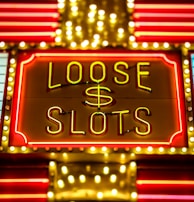 Bright neon lights display the words 'Loose Slots' with a dollar sign in the center. The sign is outlined with bulbs, creating a vibrant and flashy effect typical of a casino or entertainment venue.