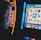 A person is closely observing a digital slot machine with colorful fruit symbols, bars, and a bell. The slot machine screen displays symbols like oranges, plums, cherries, and clouds. The background is dimly lit, creating a focused and somewhat intense atmosphere.