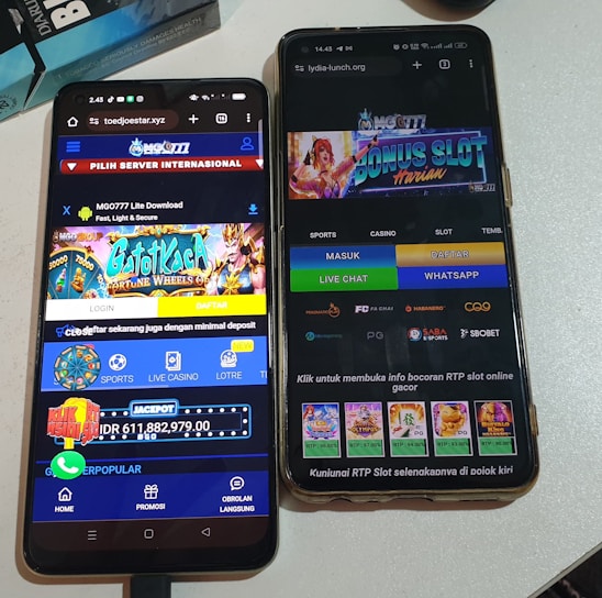 Two smartphones are displayed on a white surface, both showing gambling websites with colorful graphics, text, and various options for logging in and accessing games. The screens are bright and filled with promotional content related to casino and slot games.
